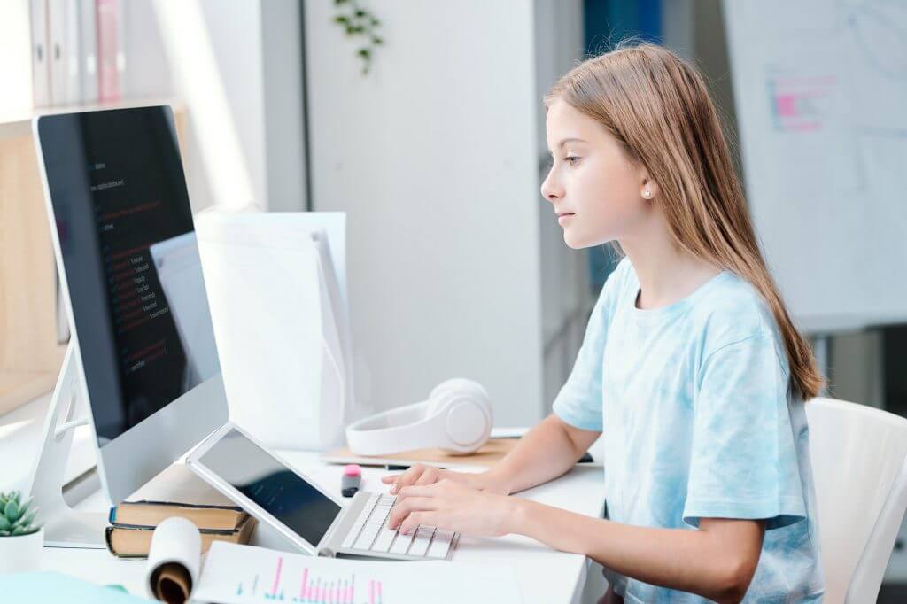 Serious clever schoolgirl looking at online data on computer screen